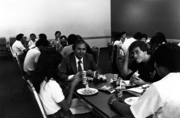 black and white candid photo of Tomas Rivera eating lunch with a group of students